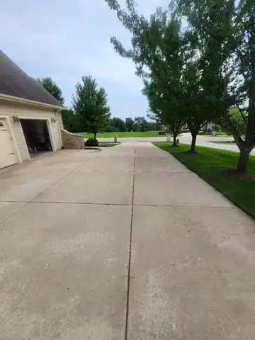 Wide clean concrete driveway beside a house and green lawn